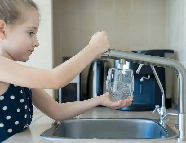 Çocuğun elinde şeffaf bir cam var. Bardak içeceği dolduruyorum. Taze içki dolduruyorum. Musluk suyu tüketimi plastik şişelerde suyun korunmasına ve çevrenin korunmasına katkıda bulunur.