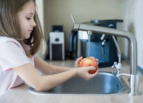 Child washing fresh apple in running water in kitchen sink. Sanitizing fruits and vegetables before eating. Hygiene concept. Disinfection of products from the store. Coronavirus infection prevention