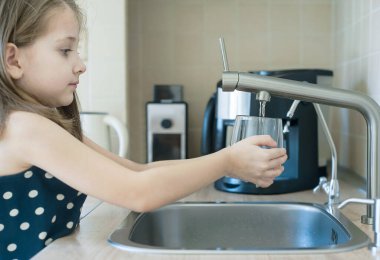 Çocuğun elinde şeffaf bir cam var. Bardak içeceği dolduruyorum. Taze içki dolduruyorum. Musluk suyu tüketimi plastik şişelerde suyun korunmasına ve çevrenin korunmasına katkıda bulunur.