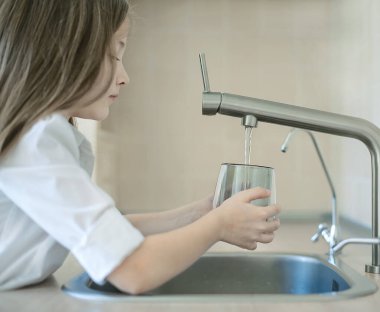 Çocuğun elinde şeffaf bir cam var. Bardak içeceği dolduruyorum. Taze içki dolduruyorum. Musluk suyu tüketimi plastik şişelerde suyun korunmasına ve çevrenin korunmasına katkıda bulunur.