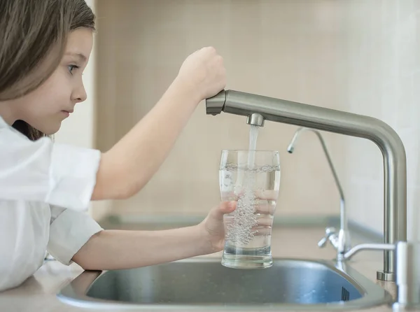 Çocuğun elinde şeffaf bir cam var. Bardak içeceği dolduruyorum. Taze içki dolduruyorum. Musluk suyu tüketimi plastik şişelerde suyun korunmasına ve çevrenin korunmasına katkıda bulunur.