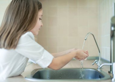 Evdeki mutfakta taze ters osmoz döken çocuk arıtılmış su. Musluk suyu içmek. Musluk suyu tüketimi plastik şişelerde su tasarrufuna katkıda bulunur. Çevreyi koruma