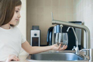 Çocuğun elinde şeffaf bir cam var. Bardak içeceği dolduruyorum. Taze içki dolduruyorum. Musluk suyu tüketimi plastik şişelerde suyun korunmasına ve çevrenin korunmasına katkıda bulunur.