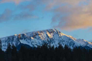 Gün batımı gökyüzü ve karla kaplı kayalık dağlar