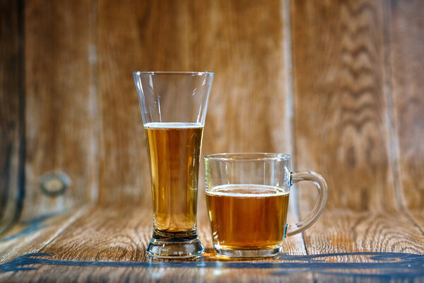          A glass and a mug of tasty beer stand on a brown background with cheese and nuts. Fragrant beer lit by beautiful light stimulates appetite.                      