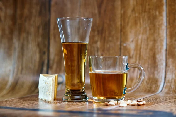          Peynir ve fındıklı kahverengi arka planda bir bardak ve bir kupa lezzetli bira standı. Güzel ışığın yaktığı mis kokulu bira iştahı açar..                      