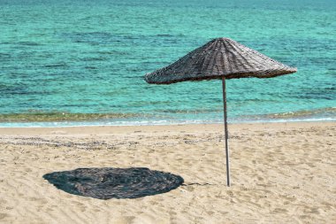 Yeşil deniz suyu yakınındaki kum plajındaki örgülü hasır şemsiye