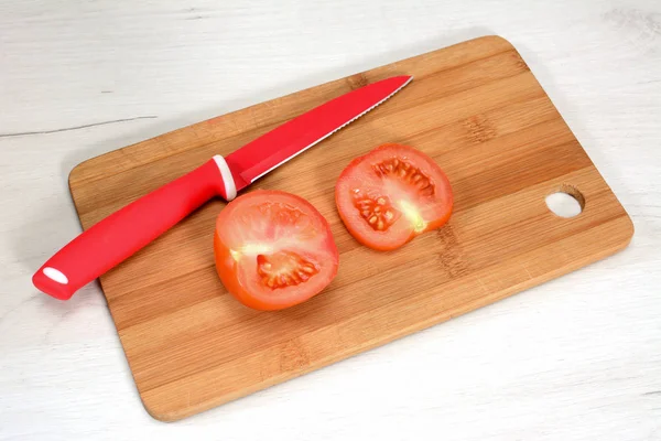 Sliced tomato on cutting board with the red special tomato knife on a white wooden table.