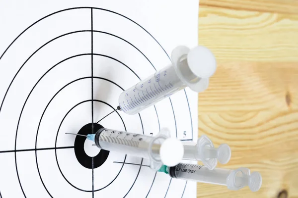 Four medical syringe hit the center of rifle target. On the wooden background. Humor concept of therapy.