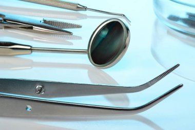 Diş hekimi ekipmanları: Diş aynası, kaşif, kornzange, pens, Petri kabında diş yanıkları. Mavi parlak yüzeyde diş aletleri, yakın plan.