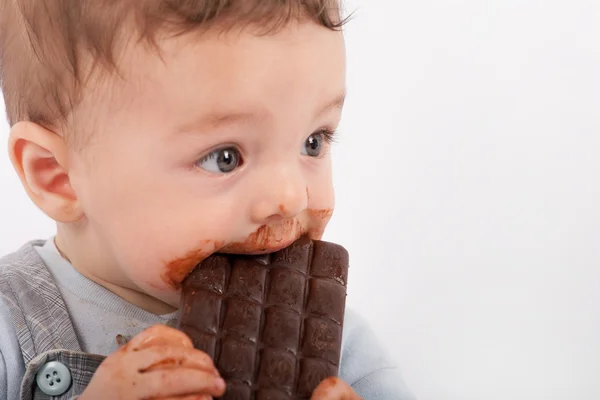 Portrait of an adorable baby boy eating a plate of chocolate. — Stock Photo, Image