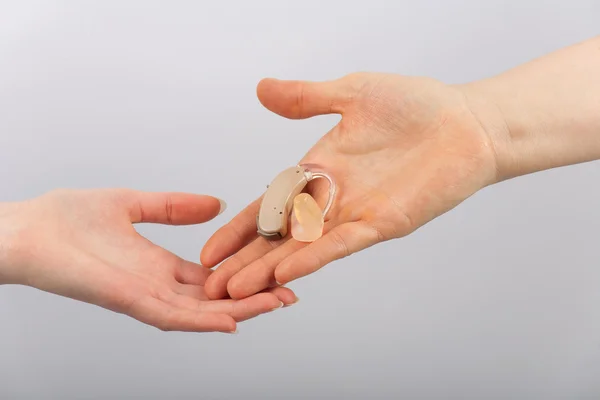 Hand giving a hearing aid to another hand — Stock Photo, Image