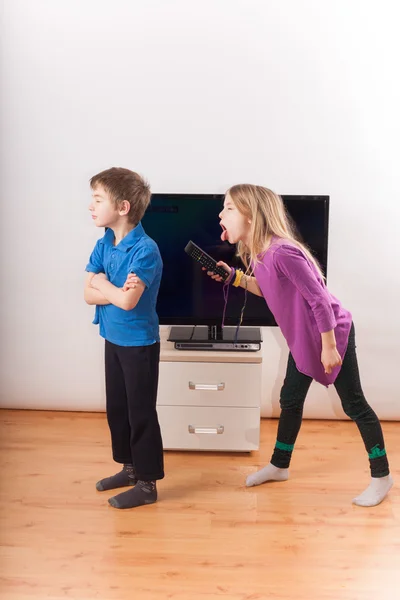 Братья и сестры конфликтуют из-за пульта дистанционного управления перед телевизором — стоковое фото