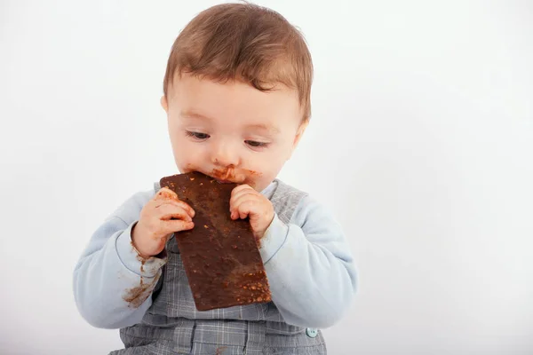 Adorable baby eating a plate of chocolate. Studio isolated on wh — Stock Photo, Image