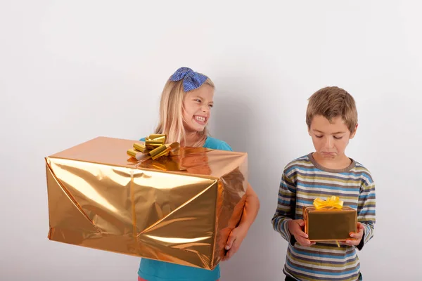 Chica joven con caja de regalo grande regodeándose sobre su hermano y su s —  Fotos de Stock