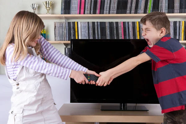 Geschwister streiten vor dem Fernseher um die Fernbedienung — Stockfoto