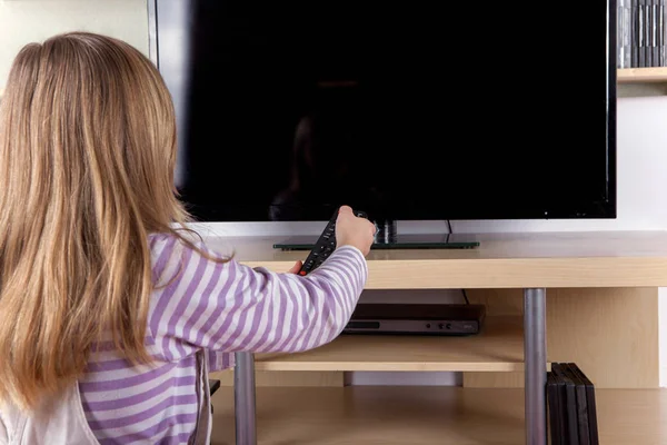 Roztomilá dívka zapnutí nebo vypnutí televize s dálkovým ovládáním — Stock fotografie