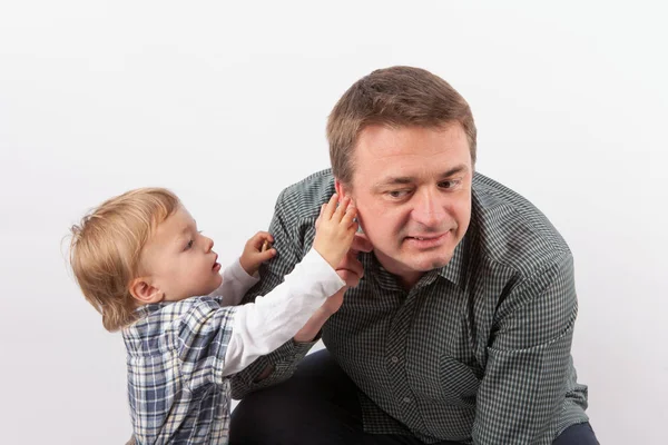 Niño pequeño inspeccionando el audífono de su padre en su oído — Foto de Stock