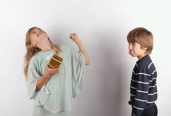 Happy girl with gift and an angry boy streching out her tongue — Stock Photo, Image