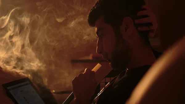 Человек курит кальян и использует планшет — стоковое фото