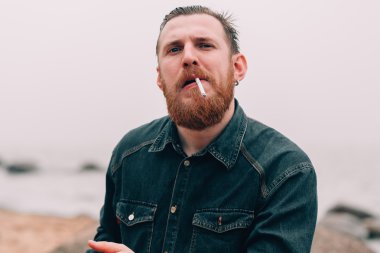 Ciddi sakallı adam sahilde bir sigara sigara