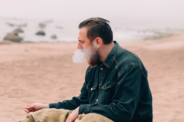 Vážnou vousatý muž s cigaretou na pláži — Stock fotografie