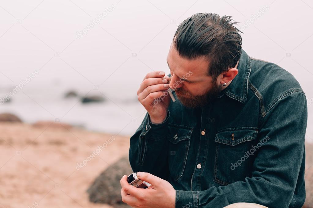 Serious bearded man smoking a cigarette on the beach