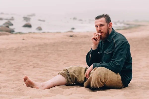 Vážnou vousatý muž s cigaretou na pláži — Stock fotografie