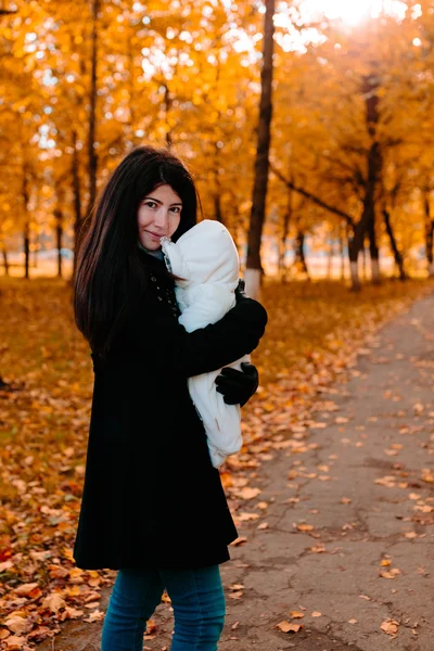 Молодая мама со своим малышом под рукой в осеннем парке — стоковое фото