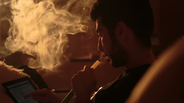 Чоловік курить кальян і використовує планшет — стокове відео