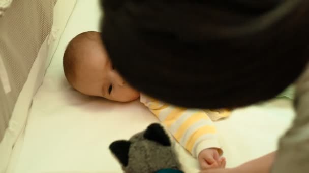 Милый новорожденный ребенок играет с плюшевой игрушкой в своей кроватке — стоковое видео