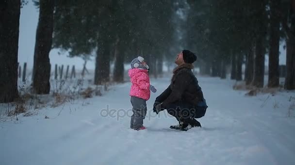 Батько зі своєю маленькою донькою насолоджується падаючим снігом взимку в парку — стокове відео