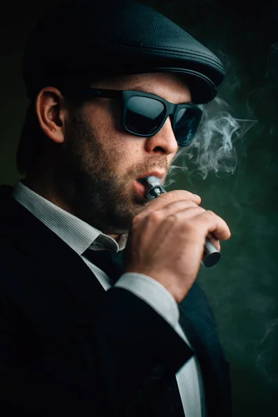 Модный мужчина в солнечных очках и кожаной кепке курит — стоковое фото