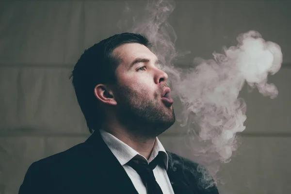 Бизнесмен выдыхает сигаретный дым — стоковое фото