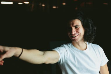 Güzel uzun saçlı esmer adam beyaz t-shirt elini doğru gösterir