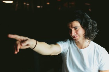 Güzel uzun saçlı esmer adam beyaz t-shirt elini doğru gösterir