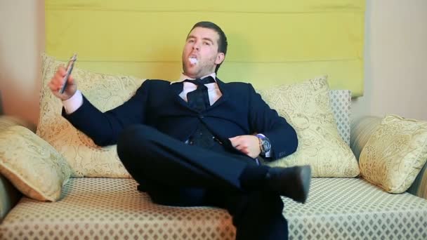 Un jeune homme d'affaires élégant fume une cigarette électronique sur un canapé — Video