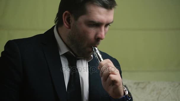 Κομψό νεαρό επιχειρηματία καπνίζει ηλεκτρονικό τσιγάρο γκρο πλαν σε έναν καναπέ — Αρχείο Βίντεο