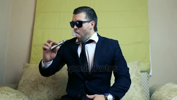 Jovem empresário elegante fuma um cigarro eletrônico em um sofá — Vídeo de Stock