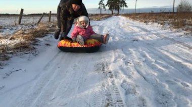 Baba kızını bir lastik şişme kar tüp iter.