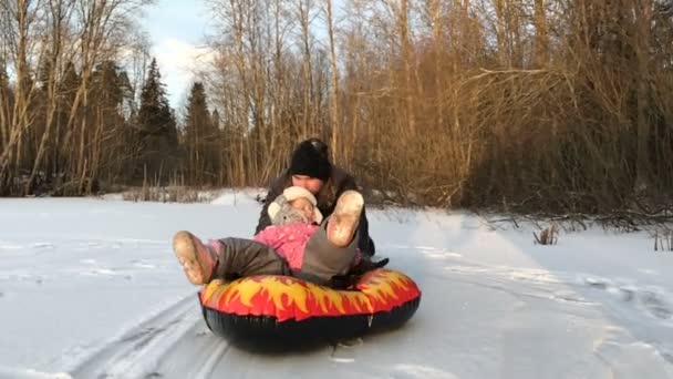 Papá empuja a su hija en un tubo de nieve inflable de goma — Vídeo de stock