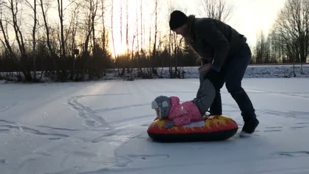 Papai empurra sua filha em um tubo de neve inflável de borracha — Vídeo de Stock