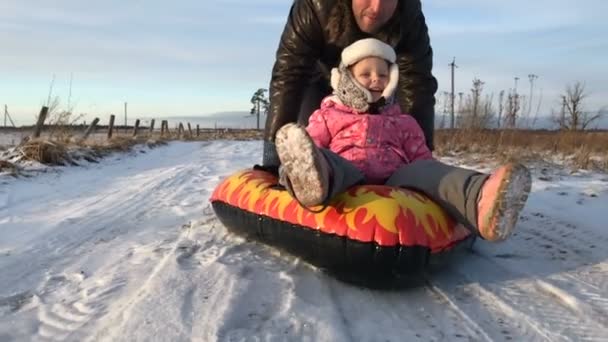 Papá empuja a su hija en un tubo de nieve inflable de goma — Vídeos de Stock