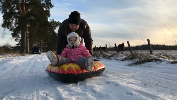 Papá empuja a su hija en un tubo de nieve inflable de goma — Vídeos de Stock