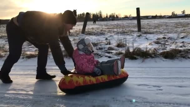 Papá empuja a su hija en un tubo de nieve inflable de goma — Vídeos de Stock