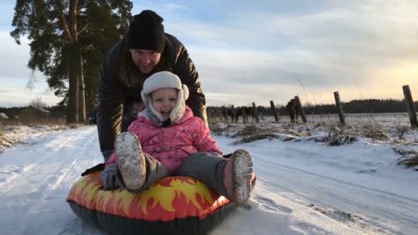 Papá empuja a su hija en un tubo de nieve inflable de goma — Vídeos de Stock