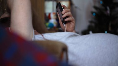 Orta yaşlı adam kanepede yatan ve Gadget'ınız müzik dinlemek