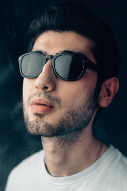 Güneş gözlüklü dumanlı bir arka plan üzerinde Ermeni şık adam. Dikey stüdyo yakın çekim portre.