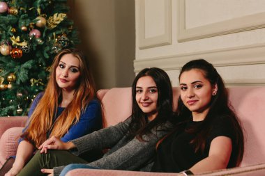 Üç güzel genç kız kanepe üzerinde Noel ağacının yakınında. Stüdyo yatay dikey.