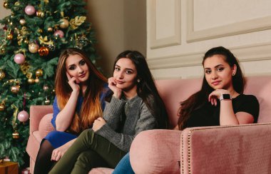 Üç güzel genç kız kanepe üzerinde Noel ağacının yakınında. Stüdyo yatay dikey.